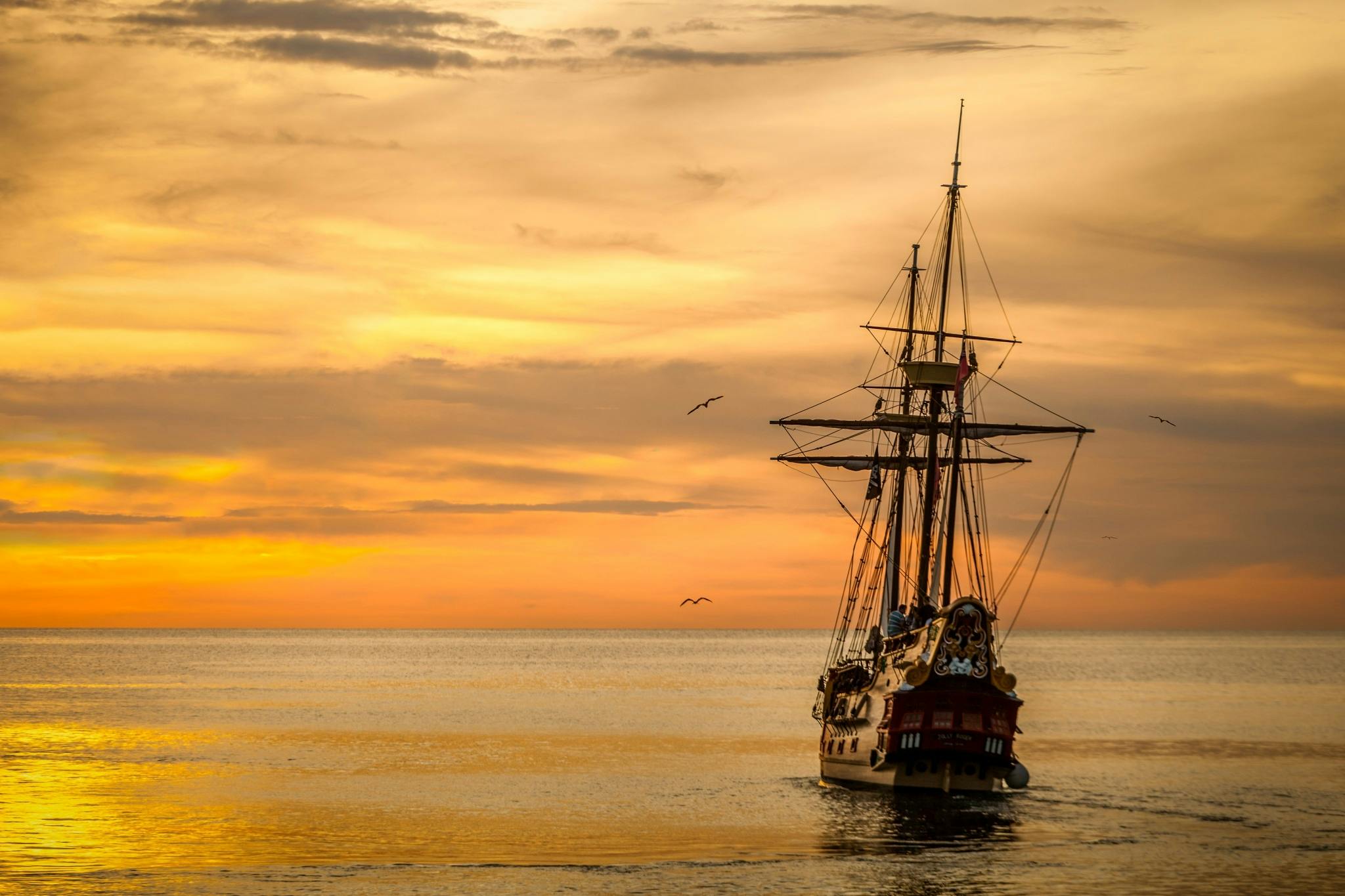 A majestic pirate ship sails into the serene waters at sunset, casting a dramatic silhouette.